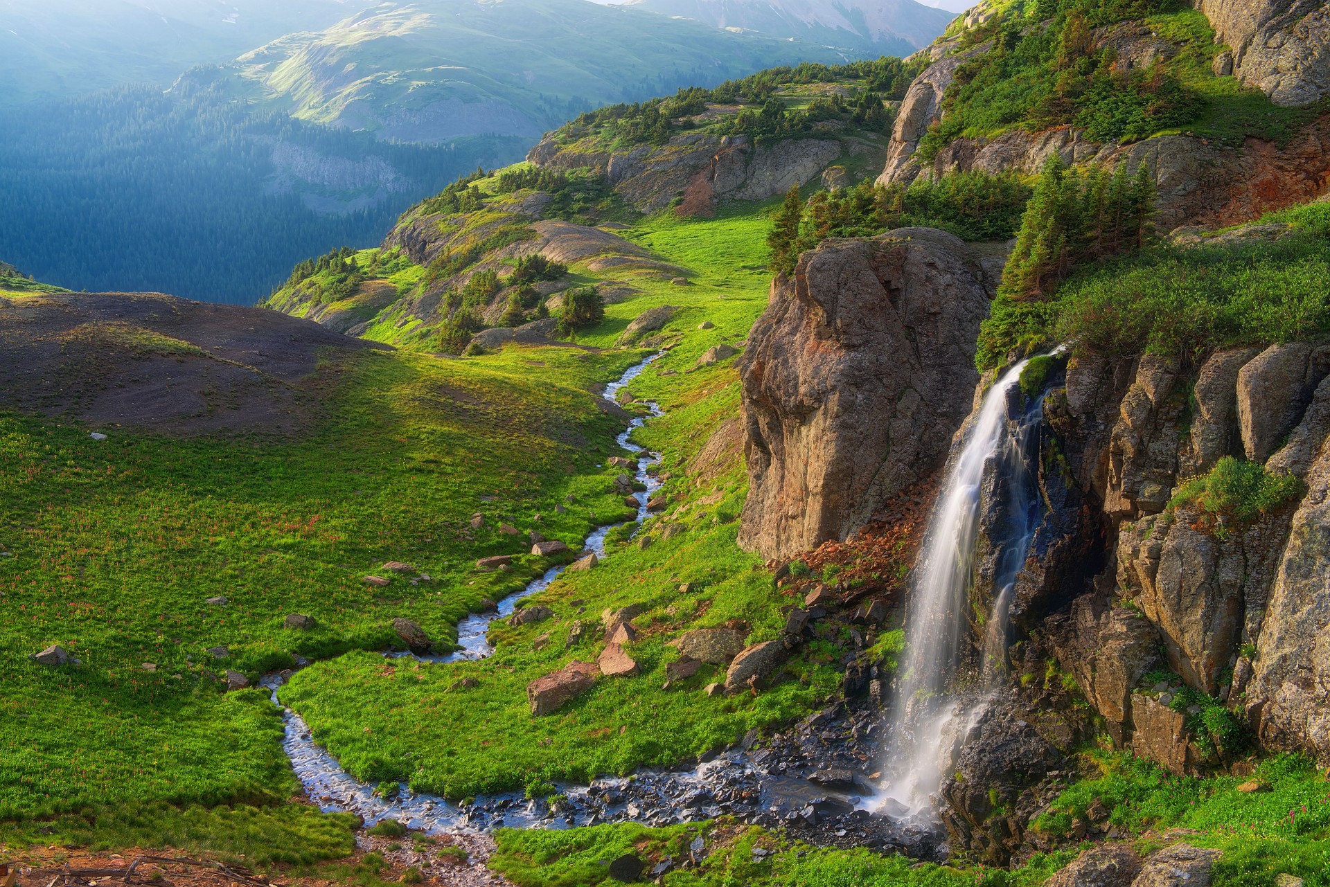 Waterfall cascades between rocky cliffs into a valley below